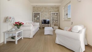 A modern living room with a flat-screen TV, white sofas, a coffee table, and built-in shelving. - L'Attico di Alessia by Perle di Puglia (Maruggio)