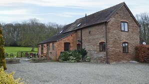 A stone building with a sloped roof, a gravel driveway, and a fenced outdoor seating area.