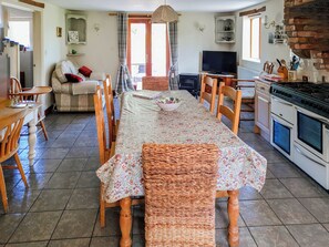 Un espace repas comprenant une longue table, des chaises, un canapé, un téléviseur et une cuisine équipée d’une cuisinière.