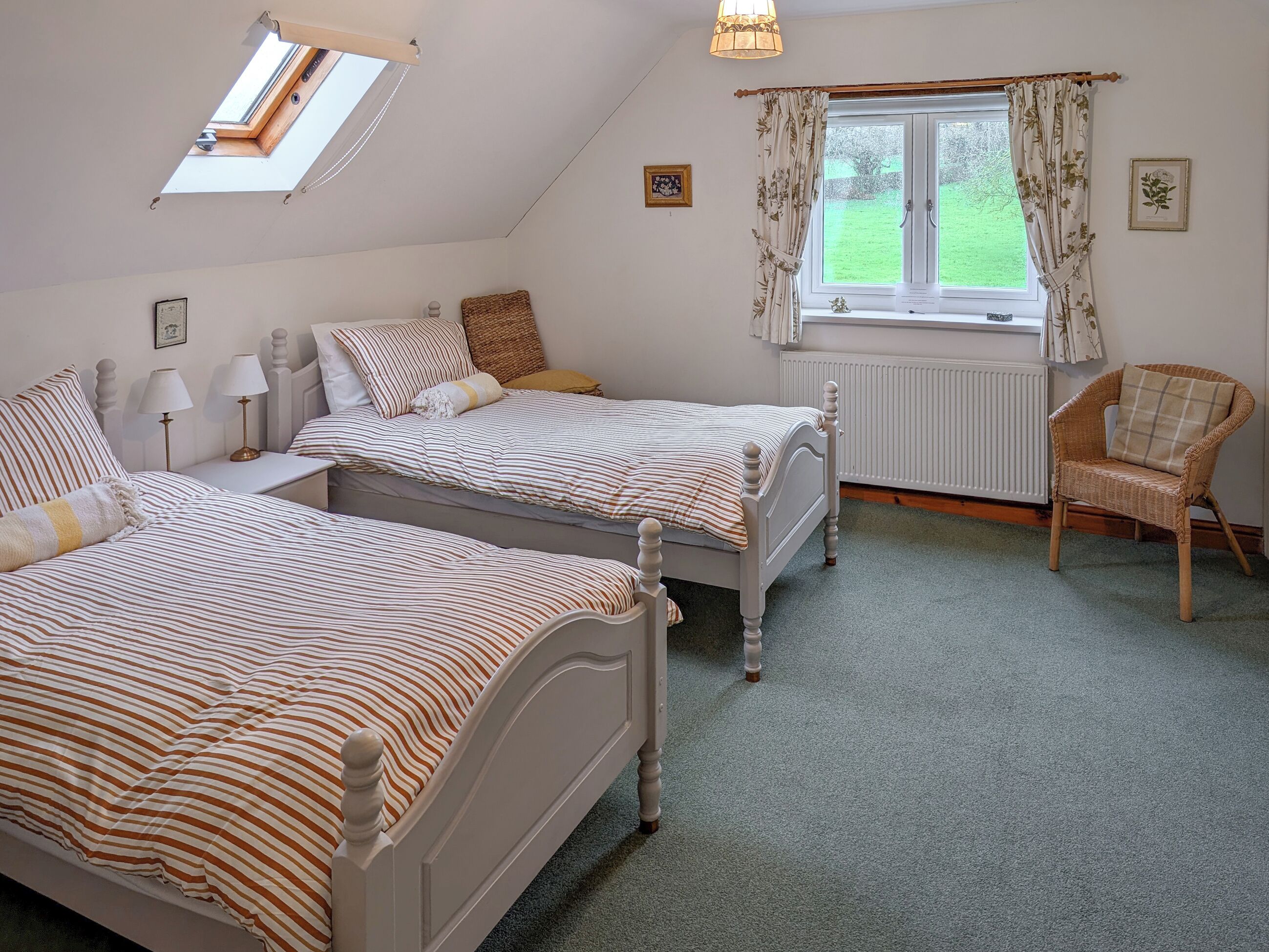 A bedroom with two beds, a window with curtains, a radiator, a chair, and a skylight.