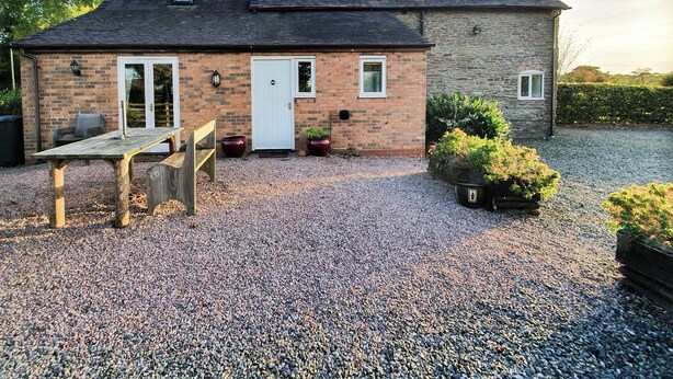 A two-story house with a gravel driveway, a wooden bench, and potted plants.