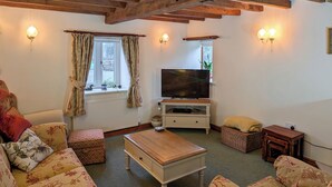 A cozy living room with floral-patterned sofas, a wooden coffee table, a television on a stand, and wall-mounted lights.