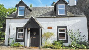 A two-story house with a dark front door, a small porch, and a gravel driveway. - Craigdarroch Cottage (Strathyre near Callander)