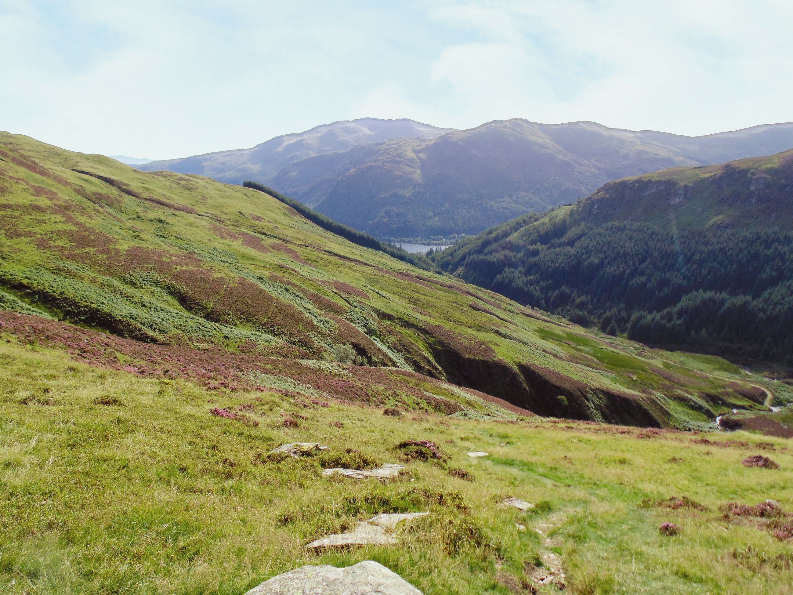 A mountainous landscape with a valley and a lake in the distance.