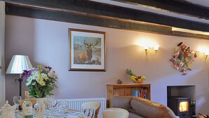 A cozy living room with a fireplace, a dining table set for tea, and a bookshelf. - Craigdarroch Cottage (Strathyre near Callander)