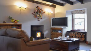 A cozy living room with a fireplace, leather sofa, wooden coffee table, and a television. - Craigdarroch Cottage (Strathyre near Callander)
