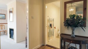 A hallway with a wooden floor, a mirror, a vase with flowers, and a wicker basket.
