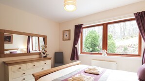 A bedroom with a bed, a dresser, a mirror, a window with curtains, and a radiator.