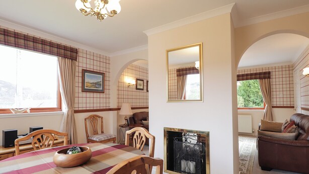 A cozy living room with a fireplace, a dining area with a checkered tablecloth, and a brown leather sofa.