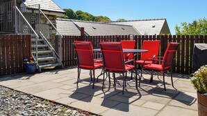 Een terras met een tafel en stoelen, een houten omheining en een trap naar een gebouw.