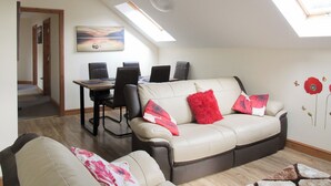 Een woonkamer met een bank, een eettafel met stoelen, een dakraam en een schilderij aan de muur.