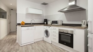 Een moderne keuken met witte kasten, een roestvrijstalen afzuigkap, een ingebouwde wasmachine en een magnetron.