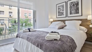 Een moderne hotelkamer met een groot bed, een balkon met uitzicht op de stad en twee ingelijste foto’s aan de muur.