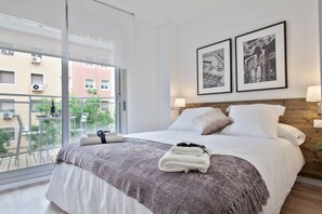 A hotel room with a large bed, a balcony with a view of buildings, and two framed pictures on the wall. - Chic Modern Flat Blanca 3 (Barcelona)