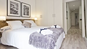 Hotelkamer met een groot bed, witte lakens, een grijze plaid en twee ingelijste foto’s aan de muur.