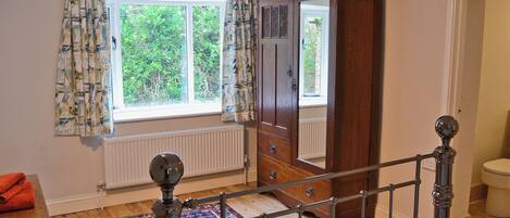 A bedroom with a large window, a wooden wardrobe, a bed, a radiator, and a red patterned rug.