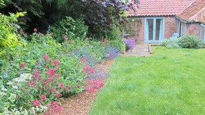 A garden with a variety of flowers and a brick house with a red roof. - 3 bedroom accommodation in Wiveton, near Cley next the Sea (Wiveton, near Cley next the Sea)
