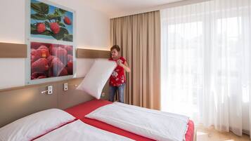 A hotel room with a bed, a large window with curtains, and a wall-mounted picture of strawberries.