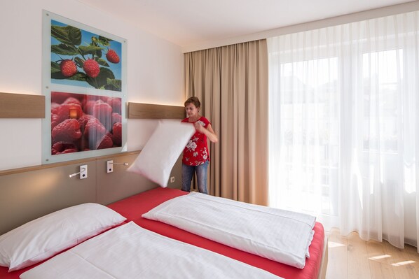 Habitación de hotel con una cama, un ventanal con cortinas y un cuadro colgado en la pared con fresas.