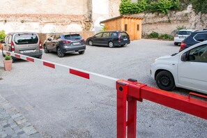 Un área de estacionamiento cerrada con varios coches aparcados, una barrera rojo y blanco, y un muro de ladrillo al fondo.