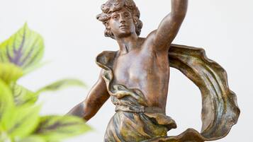 A bronze statue of a figure holding a lamp, surrounded by greenery.