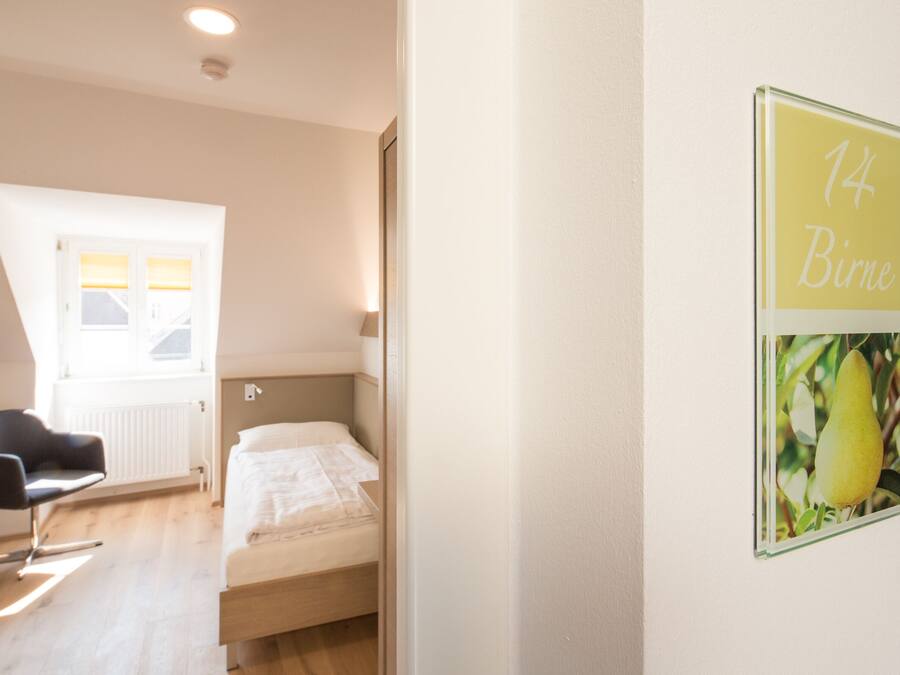 Un dormitorio con cama, una silla, un ventanal y una pared con un letrero.