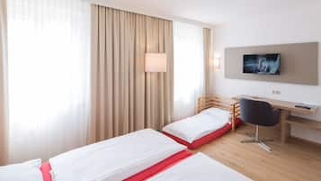 Habitación de hotel con dos camas, un escritorio, una silla, un televisor y una ventana con cortinas.