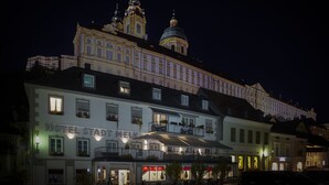 Hotel Stadthotel Melk, con un edificio destacado al fondo, balcones con jardineras y una fachada bien iluminada.