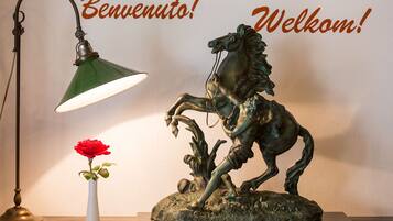A bronze horse statue on a pedestal, a green desk lamp, and a white vase with a red rose.