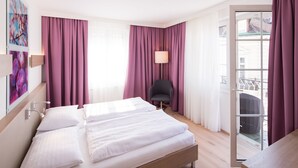 Habitación de hotel con una cama grande, una silla y un balcón con vistas.