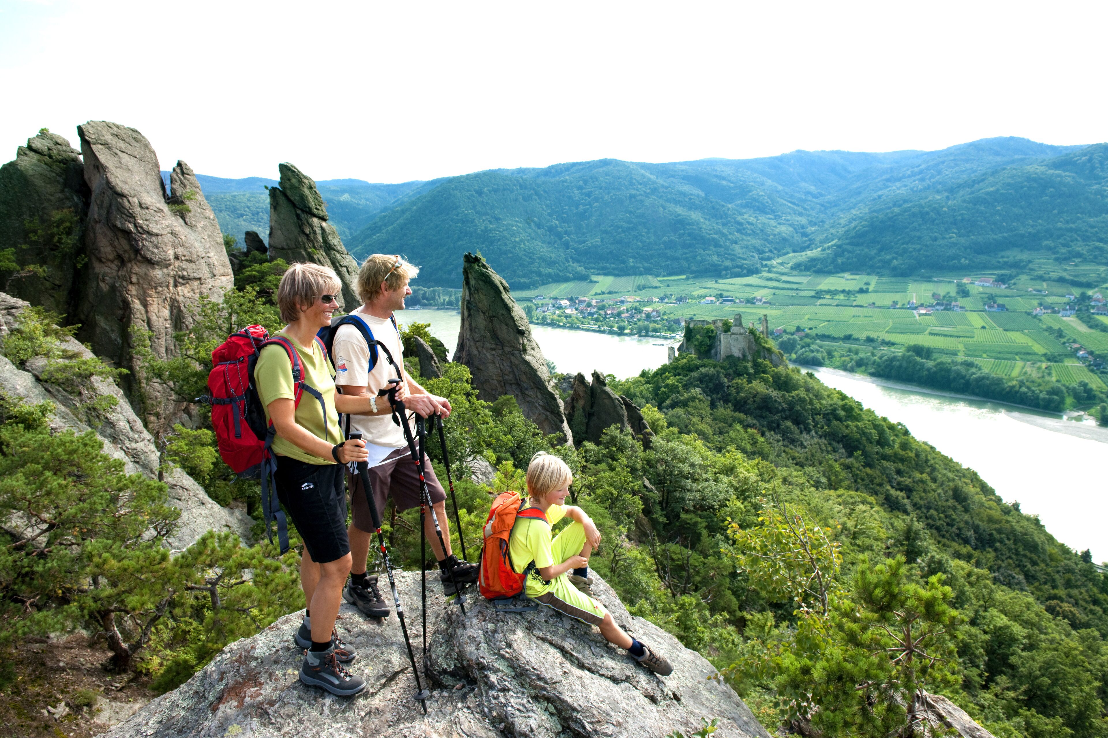 Un grupo de excursionistas en un saliente rocoso con vistas a un valle con río y pueblo distante.