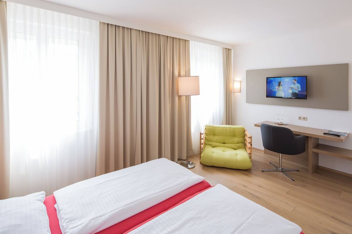 A hotel room with a bed, a desk, a chair, a TV, and curtains.