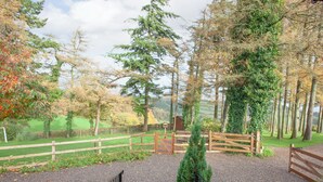 A pathway leading to a wooden gate with a small evergreen tree in the center, surrounded by gravel and a metal fence. - Challette At Timbertops (Washfield, near Tiverton)