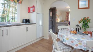A kitchen with white cabinets, a stainless steel refrigerator, and a dining area with a table set for two. - Challette At Timbertops (Washfield, near Tiverton)