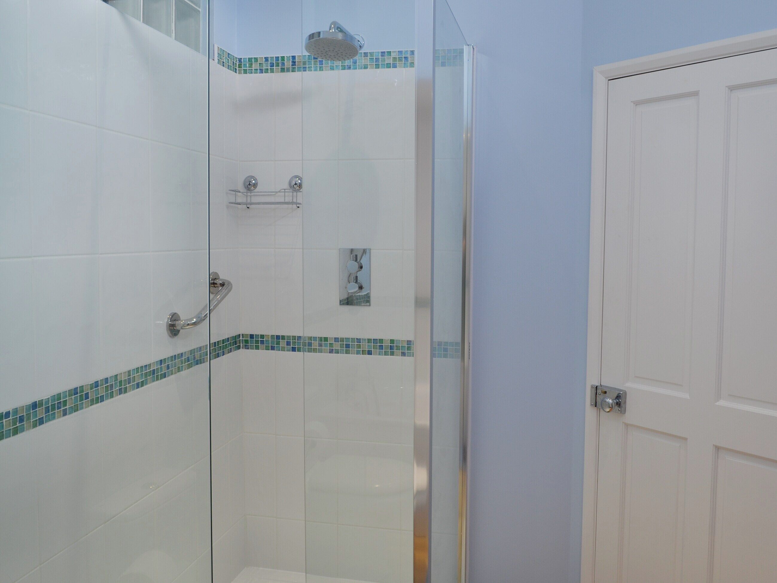 Una cabina doccia in vetro con piastrelle bianche e una cornice a mosaico blu.
