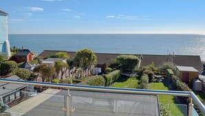 Un quartier résidentiel offrant une vue sur la mer, avec un balcon doté d’une balustrade en métal, un petit jardin et une clôture en bois.