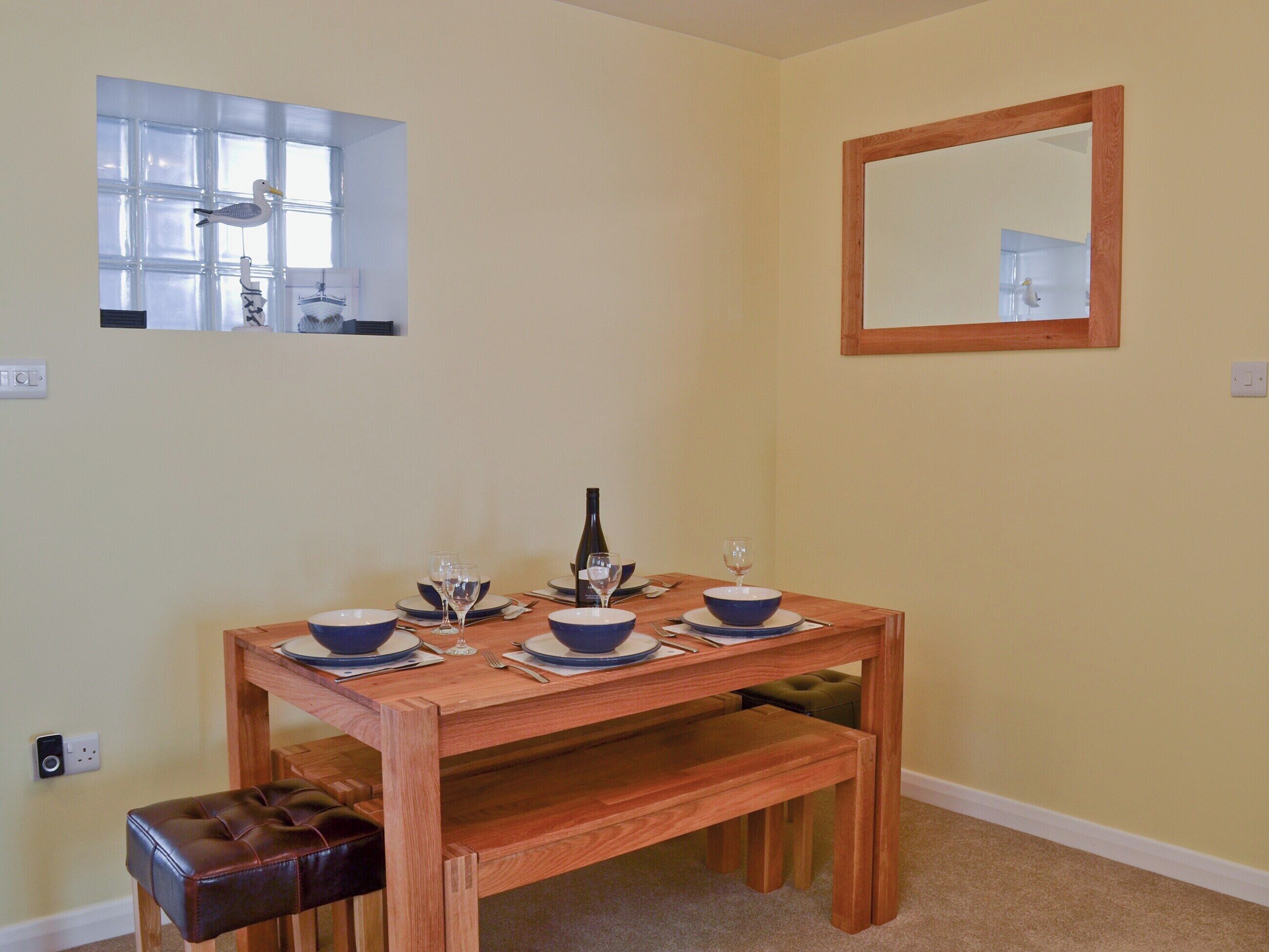 A dining table set with bowls, wine glasses, and a bottle, with a mirror and window on the walls.