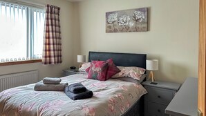 A bedroom with a bed, nightstands, a lamp, a painting, and a window with curtains. - 3 bedroom accommodation in Portree (Portree)