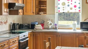 A kitchen with wooden cabinets, a gas stove, a microwave, and a window with a polka dot curtain. - 3 bedroom accommodation in Portree (Portree)