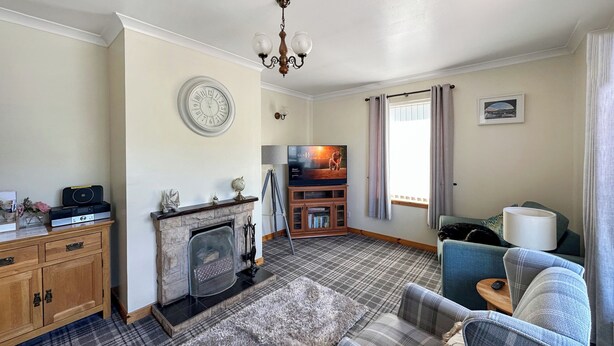 A living room with a fireplace, a television, a sofa, and a wooden cabinet. - 3 bedroom accommodation in Portree (Portree)