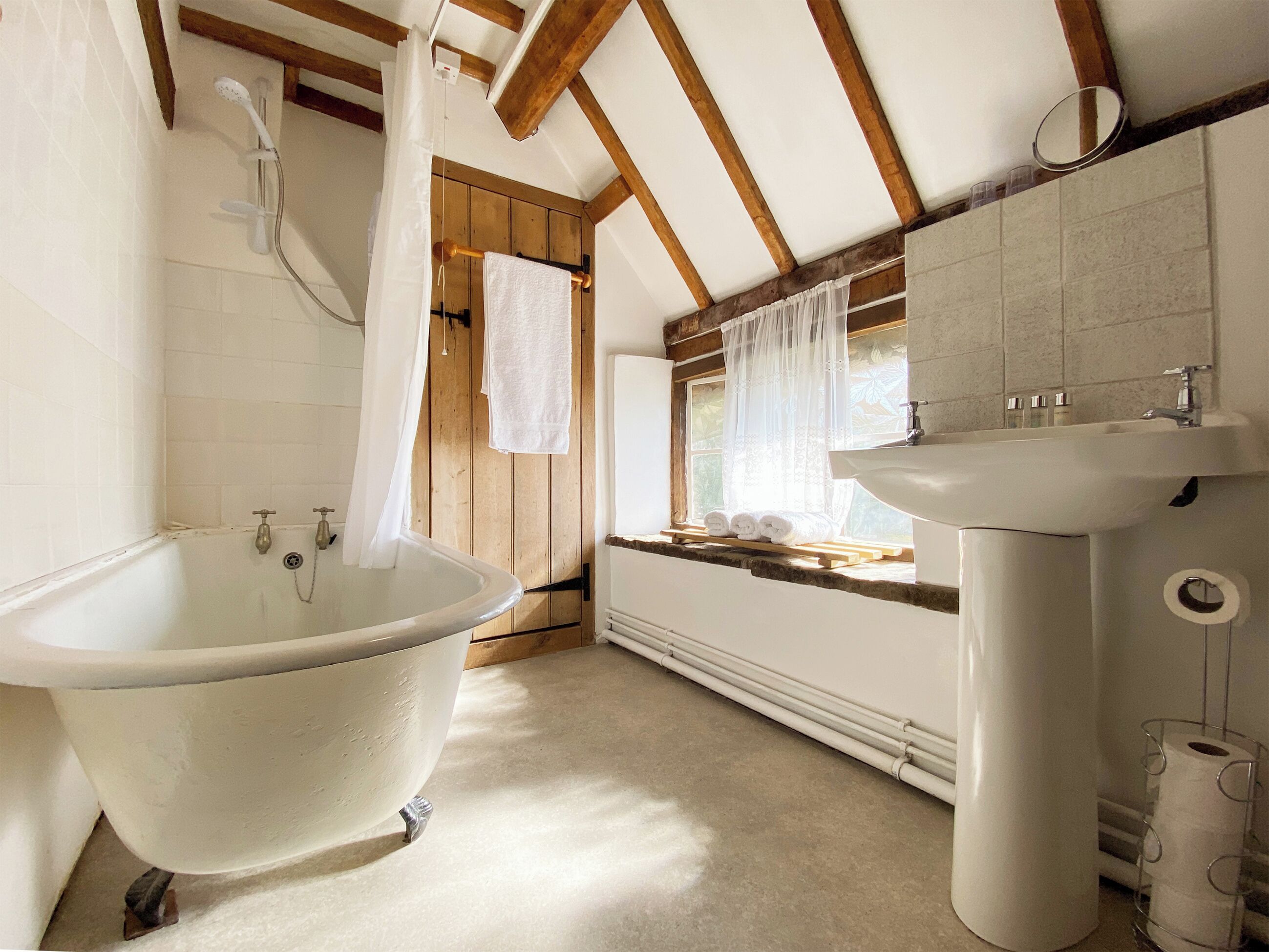 Een badkamer met een vrijstaand bad, een wastafel en een raam met gordijnen.