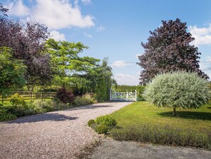 A gravel path leading to a white gate, surrounded by lush greenery and trees.