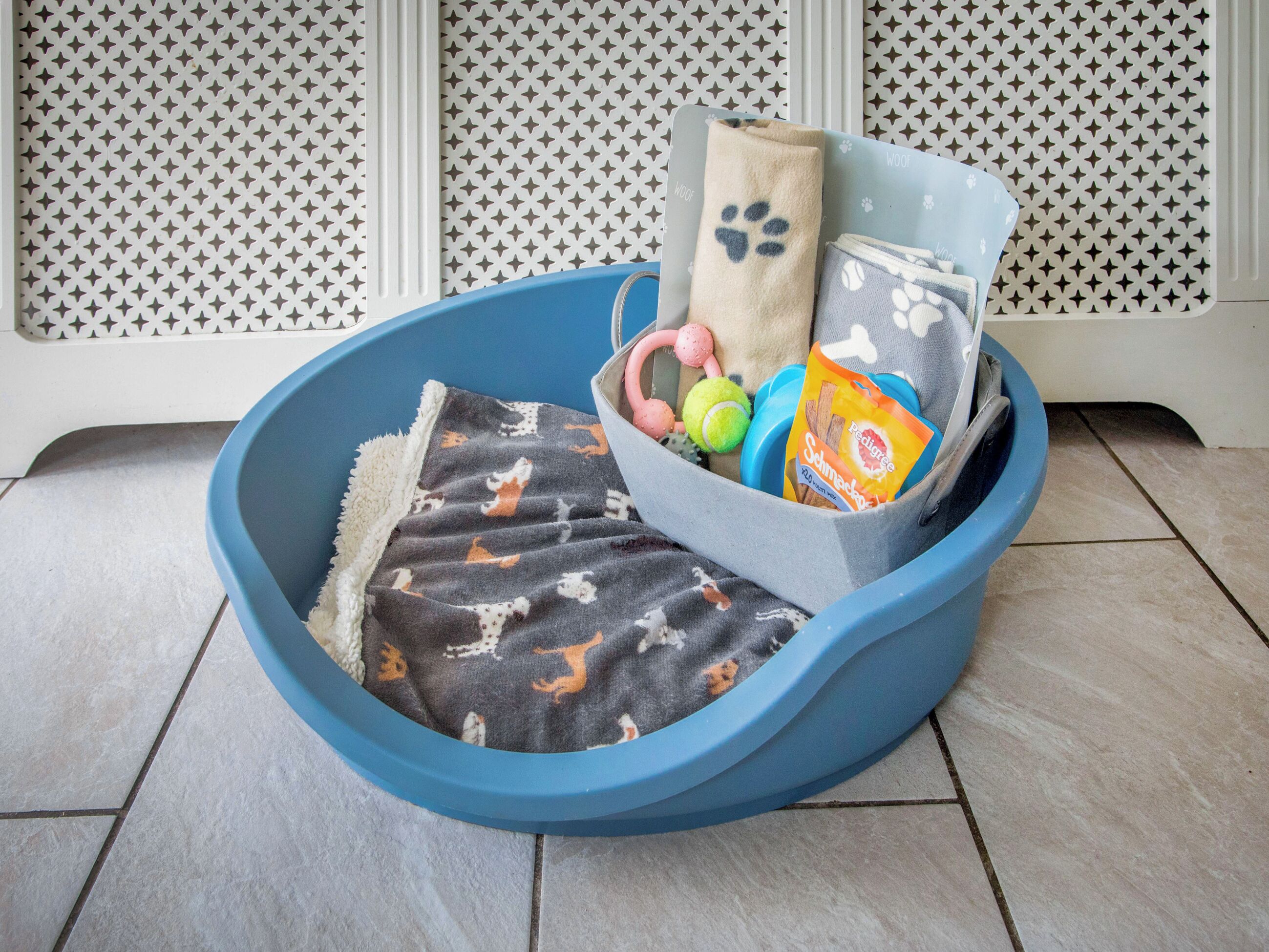 A blue pet bed with a blanket and toys.