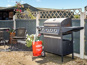 Una barbacoa amb un dipòsit de gas, una cadira de vimetla i una tanca de fusta.