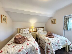 A bedroom with two beds, each with floral bedding and towels, a bedside table with a lamp, and framed pictures on the walls. - 2 bedroom accommodation in Ellesmere (Ellesmere)