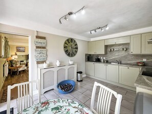 A kitchen with a microwave, sink, and cabinets, a dining area with a table and chairs, and a living room with a sofa and a painting.