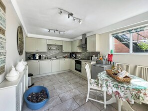 A kitchen with white cabinets, a dining table with a floral tablecloth, and a blue laundry basket.