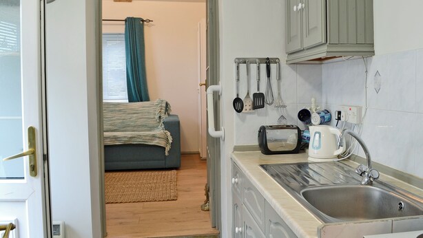 A compact kitchen with a sink, a toaster, and a kettle. There is a wooden floor and a blue sofa in the adjacent living area. - 0 bedroom accommodation in Seatown (Seatown)