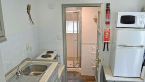 A compact kitchen with a sink, stove, and a microwave on top of a refrigerator. - 0 bedroom accommodation in Seatown (Seatown)
