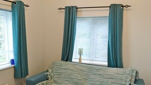 A room with a blue sofa, teal curtains, a window with blinds, and a lamp on the windowsill. - 0 bedroom accommodation in Seatown (Seatown)